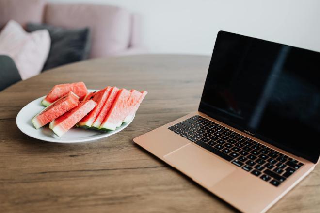 Een laptop op een tafel met daarnaast een bord met stukken watermeloen