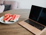 Een laptop op een tafel met daarnaast een bord met stukken watermeloen